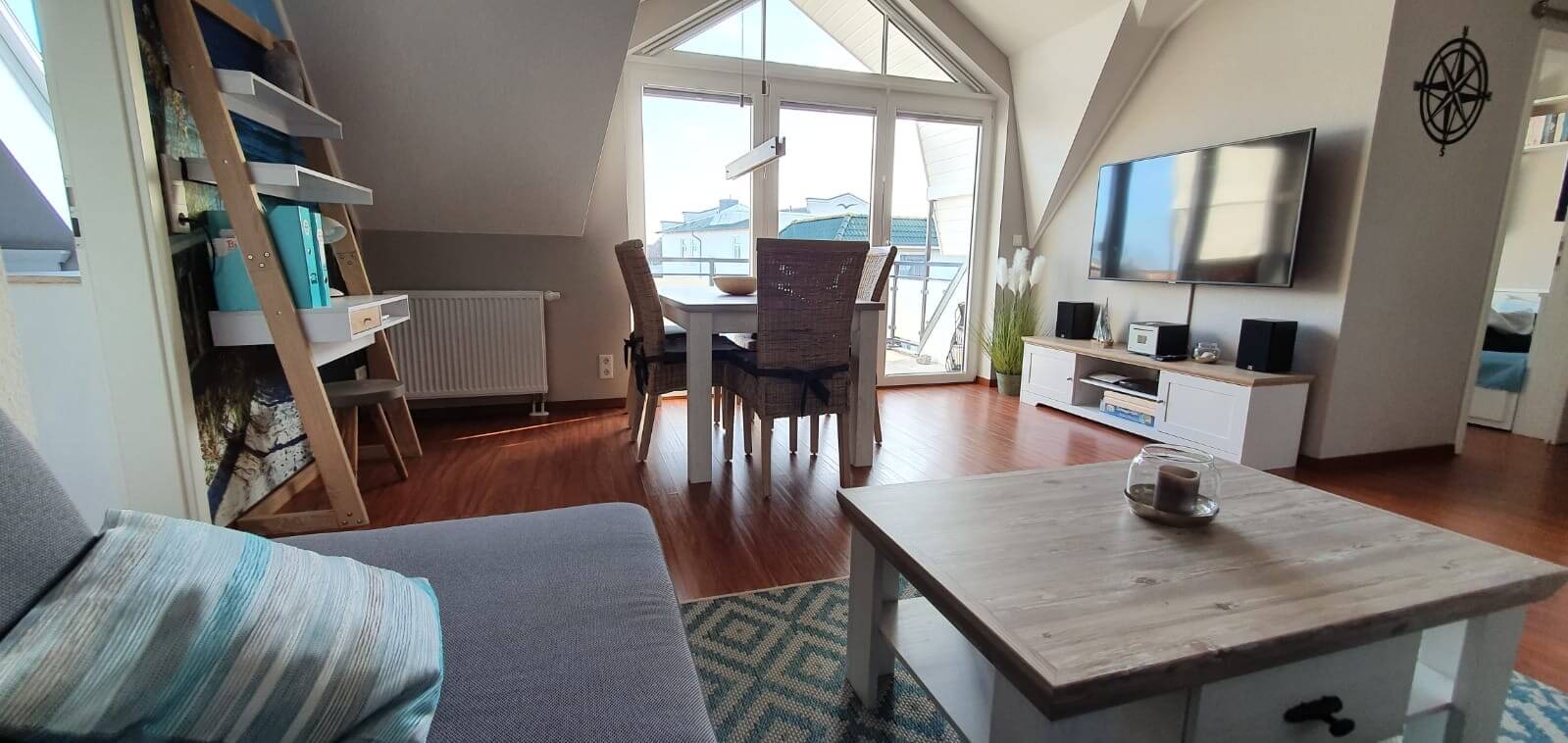 wohnzimmer_wide_top4_hero-1-1 Wohnzimmer - Blick vom Sofa zum sonnigen Balkon. Davor einladener Esstisch. Und auf der rechten Seite hängt der große LED-TV an der Wand